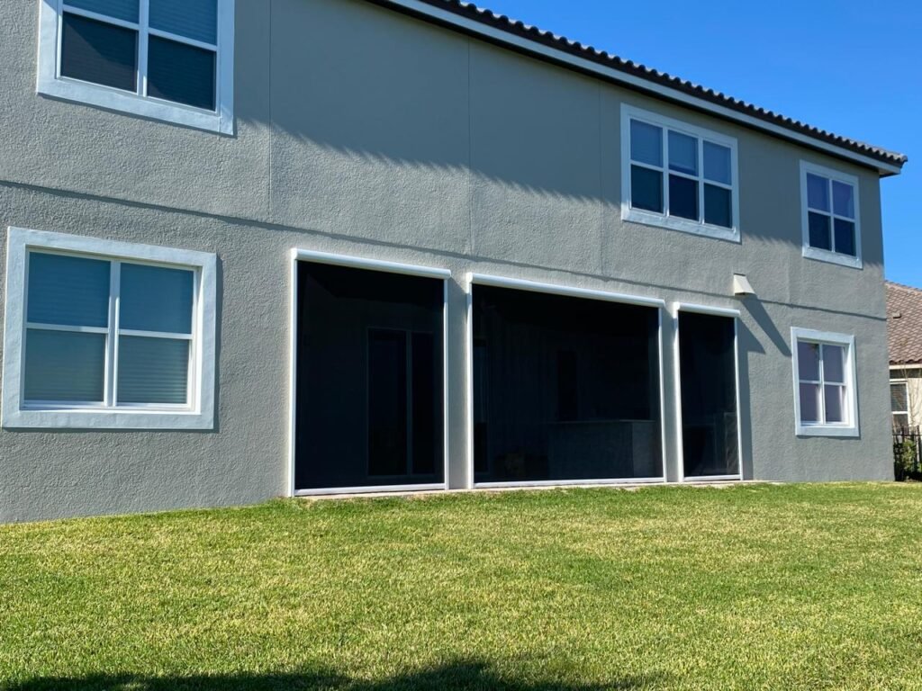 Back of a two-storey house with three outdoor shade screens lowered over the patio openings