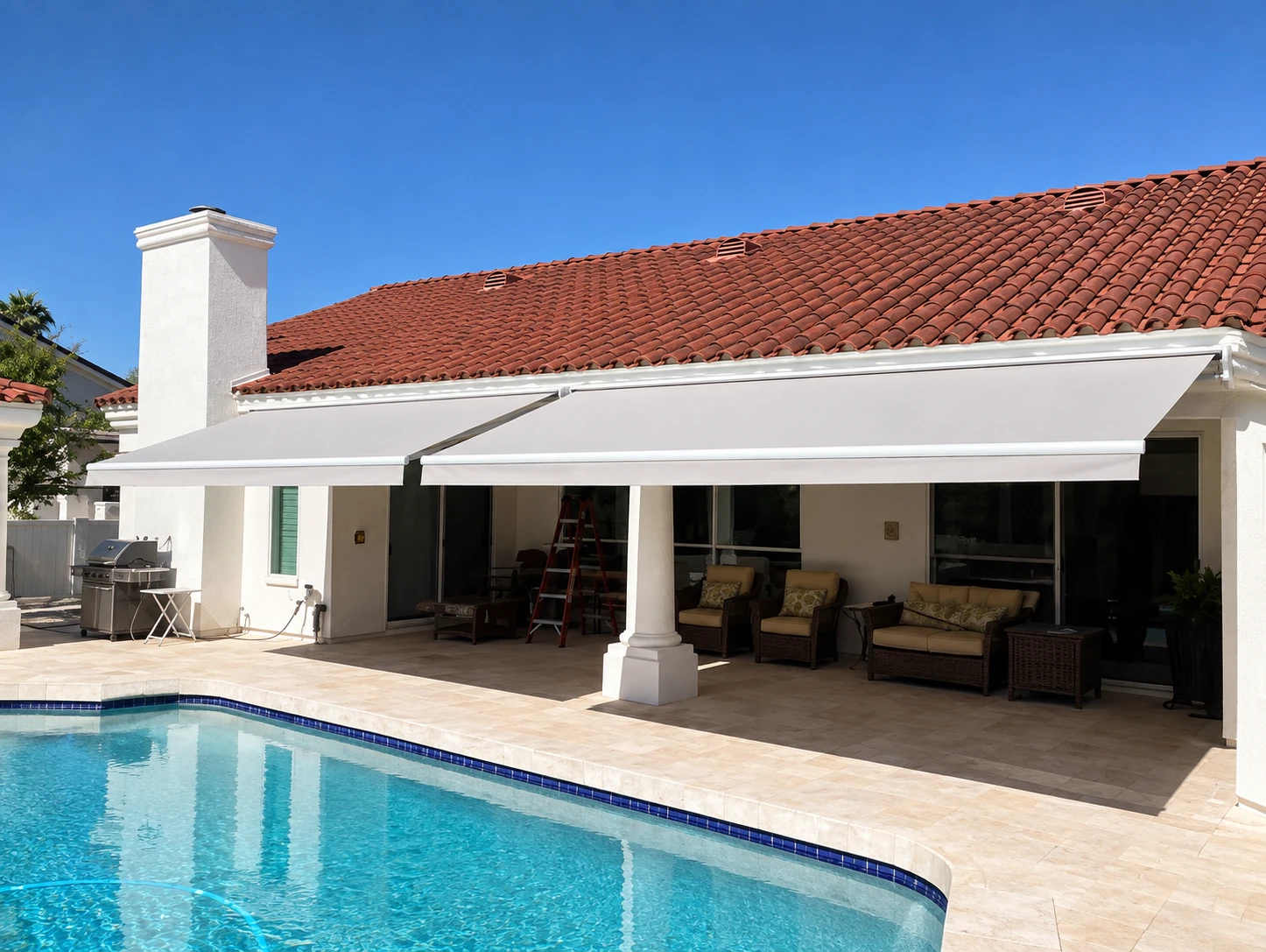 Two retractable awnings extended over a covered patio with seating, beside a pool