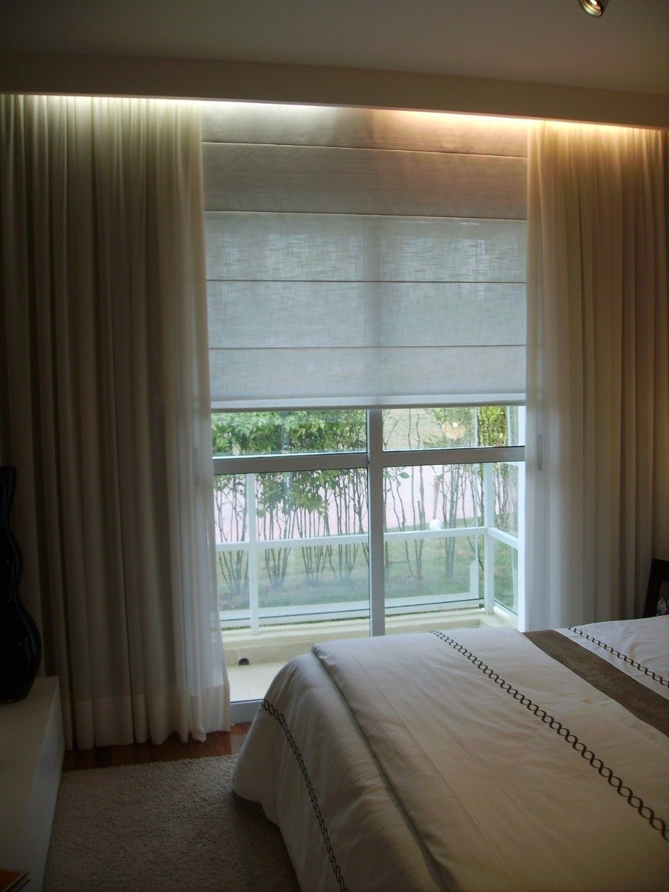 Roman shade layered with sheer curtains in a bedroom