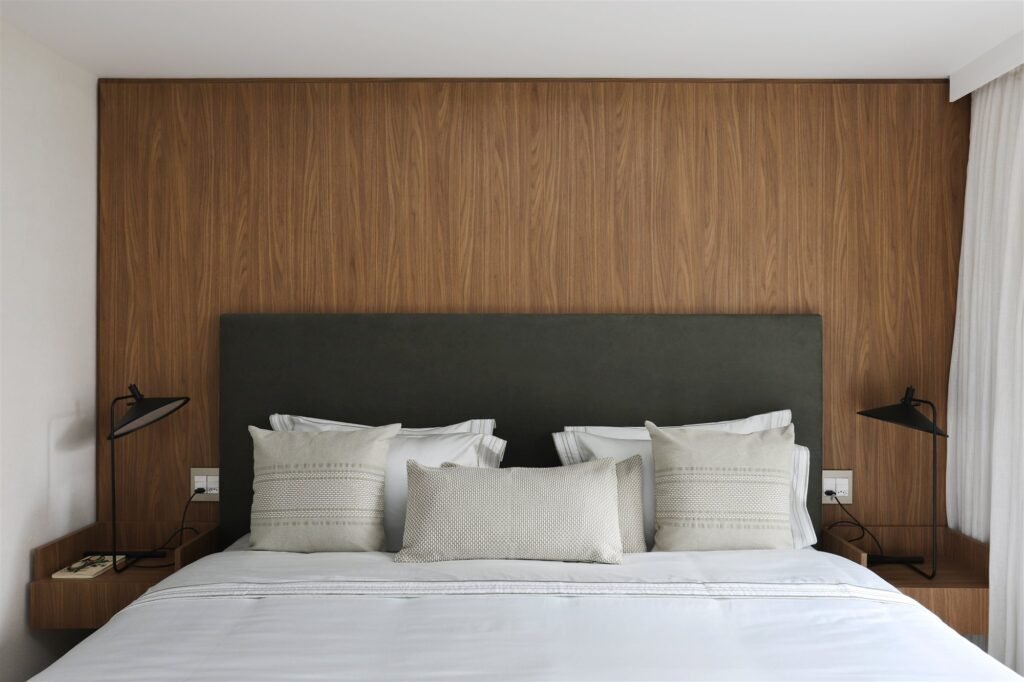 Sheer curtain beside a master bed with a wood headboard wall