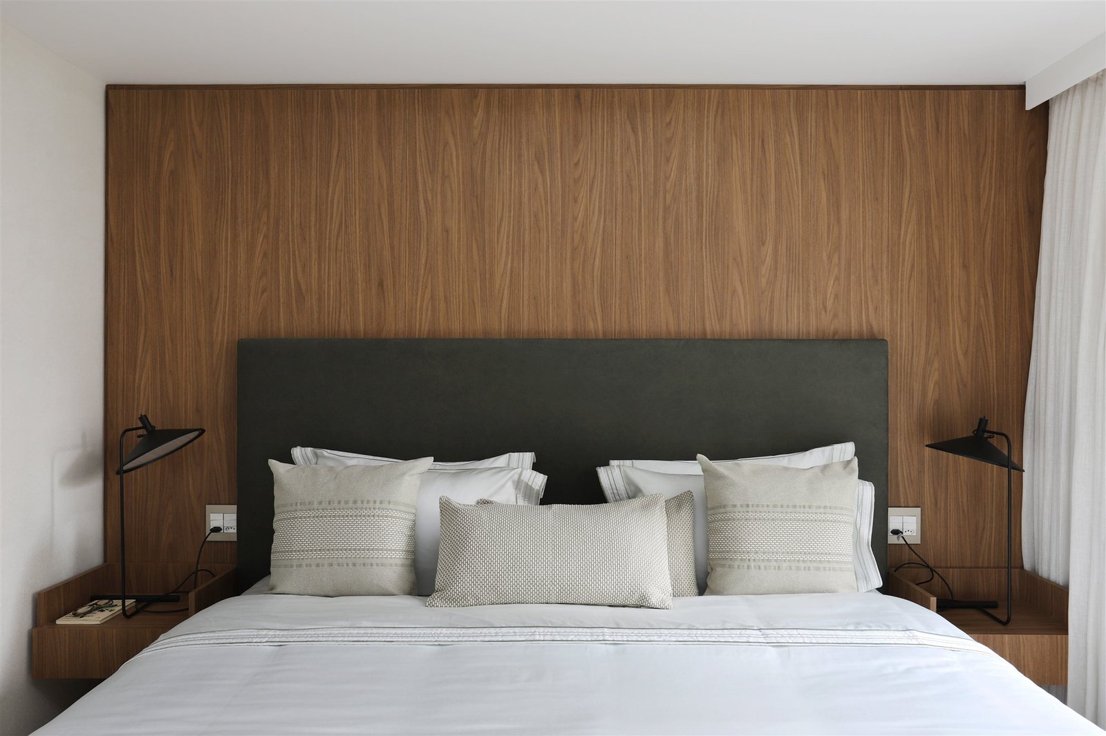 Sheer curtain beside a master bed with a wood headboard wall