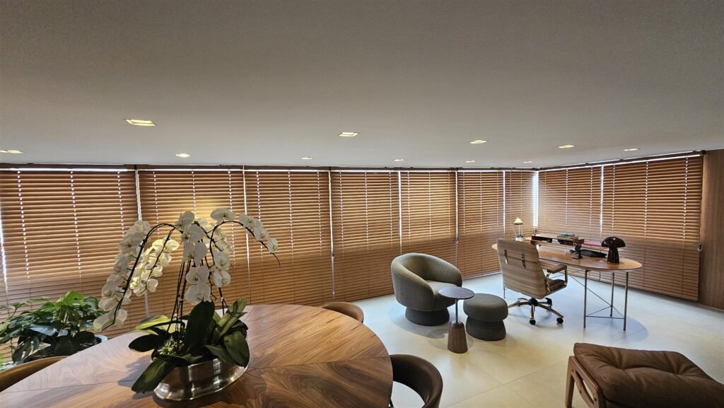 Office with wood blinds on tall windows behind a round wooden table with an orchid